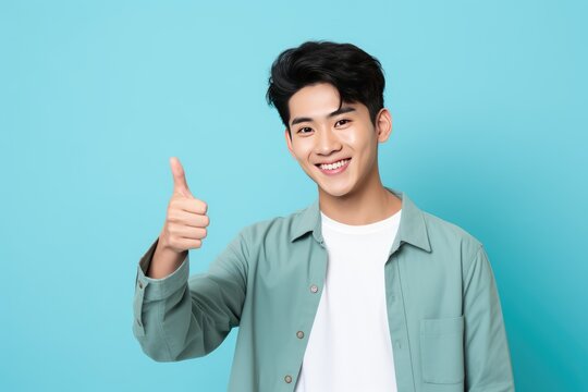 Smiling Young Asian Man Giving Thumbs-Up Against Blue Background