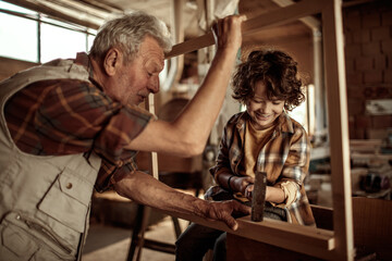 Fototapeta na wymiar Elderly carpenter making wood frame with little boy in workshop