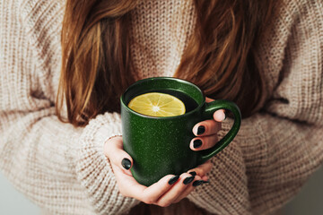 Hot tea in a mug. Woman holding mug of lemon tea. Cold winter relax background. Woolen sweater warm...