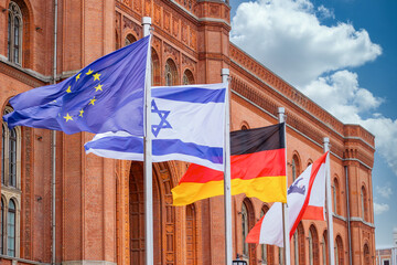 The European, Israeli, German and Berlin flags blow in the wind in front of the Berlin town hall "Red Town Hall", the sky is blue with clouds