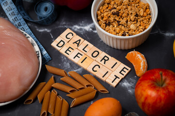 Flat lay photo showing calorie deficit. The inscription calorie deficit next to fruit, vegetables, meat and pasta. A healthy, tasty and balanced diet