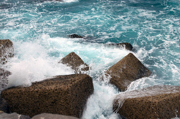 Big waves in the sea at the stone block jetty. Sea pier with breakwater stone cubes close-up view. The Tyrrhenian Sea, Cefalu, Sicily, Italy
