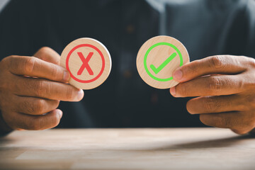 Symbolic yes or no, hand holds wooden cubes featuring a green checkmark and red cross. True and false symbols used for evaluation purposes. Think With Yes Or No Choice.