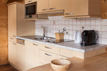 Cosy kitchenette in natural wood colour with ceramic tiles and accessories in a rustic hotel room