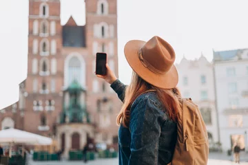 Foto op Aluminium Happy young European tourist with backpack in hat makes photo or video on smartphone on Market Square in Krakow. Traveling Europe in summer. St. Marys Basilica. Vacation concept © mdyn