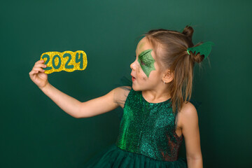 A funny girl with a drawing on her face in the shape of a dragon looks at the numbers of the 2024...