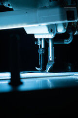 The needle with thread in the sewing machine is illuminated by cold backlight.
