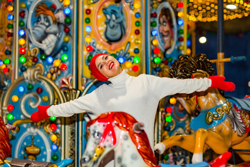 A young, beautiful woman walks in the park in an amusement park, rides on carousels, wearing a hat and winter clothes.