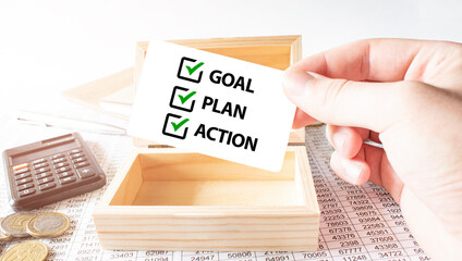 Businessman hold white card with text 2024 GOAL PLAN ACTION Calculator, wood box, money and financial documents