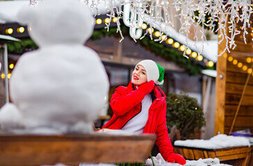 A young, beautiful woman walks through a winter city in a hat and winter clothes, among snow and snowmen