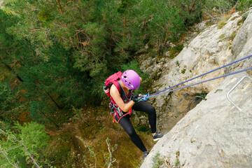 Woman initiating rappel with a forest background - obrazy, fototapety, plakaty