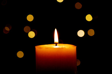 Candle burns Isolated On Black background with Christmas Lights Defocused Bokeh.