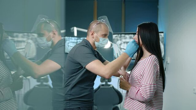 Male dentist placing tooth chart to natural teeth of female patient standing in illuminated well-equipped dentist office. Cosmetic dentistry, whitening. High quality 4k footage