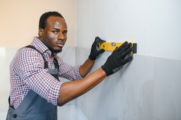 African American Worker installing wall tile with vacuum holder indoors