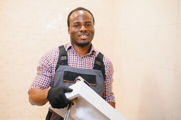 Side View Of Young African Male Plumber Fixing Sink In Bathroom