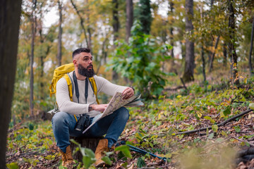Obraz premium During his woodland hike, a hipster enjoys a rest, sitting on a tree stump while consulting a paper map to plan his route.