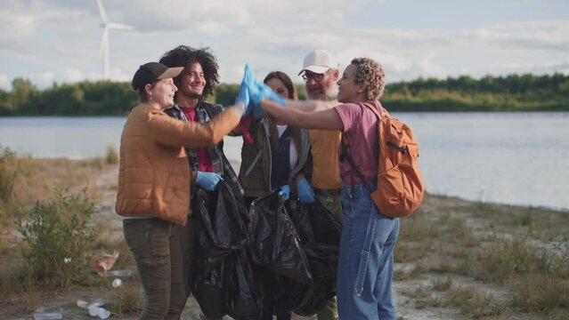 volunteers in nature park high five for the good job - group of environmentalist cleaning nature from garbage