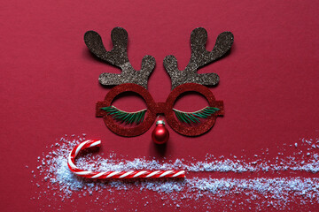 Christmas card, concept. Red background t symbol of deer, antlers, glasses and ball nose, candy stick and snow.