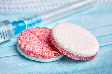 a plastic medical syringe and tablets lie on protective masks on a blue background, photographed in close-up from above at an angle,