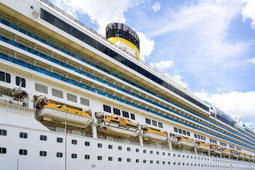 Side view of a large cruise ship with many hanging lifeboats and liferafts, blue sky background
