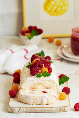 Meringue roll with butter cream and raspberry curd, decorated with berries on a light background.