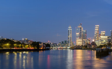 Fototapeta premium The lit urban skyline in London after sunset time with reflections in the river Thames