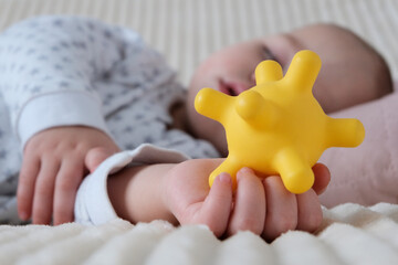 A baby is sleeping in a crib, a child of European appearance, wearing a light light jumpsuit. A yellow rubber toy in the hand. Sleep patterns for babies, care and hygiene.