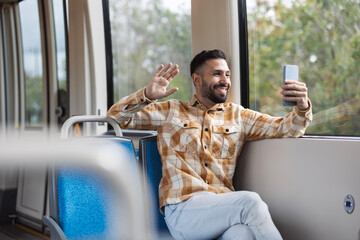 handsome latin man makes a video call with his smartphone while riding the train waving - obrazy, fototapety, plakaty
