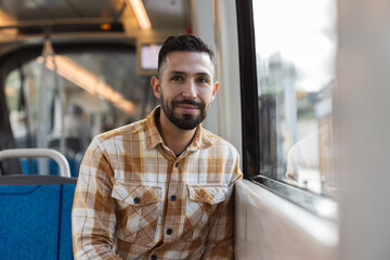 Portrait of handsome adult Hispanic man looking at camera while sitting in a train car - obrazy, fototapety, plakaty