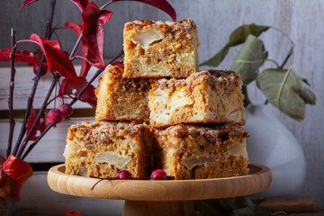 Slices of Dutch apple cake with streusel on a wooden tray, apples and apple branches on a wooden background.