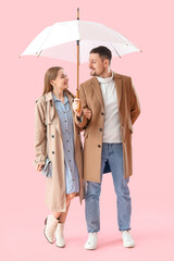 Young couple with umbrella on pink background