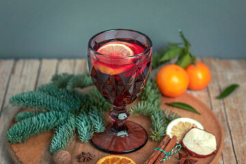 Wineglass with mulled wine on wooden tray with fruits and Christmas decorations on gray background. Closeup