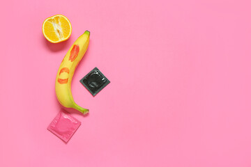 Fresh banana with lipstick kiss, orange and condoms on pink background. Sex education concept - obrazy, fototapety, plakaty