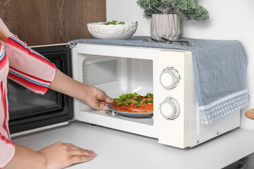 Woman preparing food in microwave oven at home