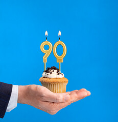 Hand delivering birthday cupcake - Candle number 90 on blue background