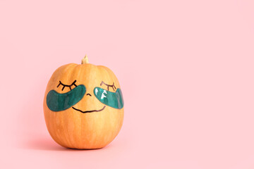 Pumpkin with drawn face and under-eye patches on pink background