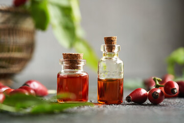 Two bottles of rose hip seed oil with fresh rosehips on a table