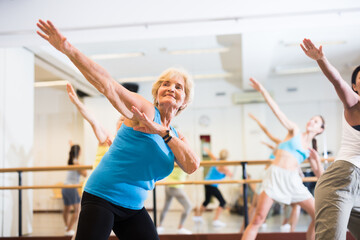 Portrait of smiling mature woman practicing ballet dance moves during group class in choreographic...