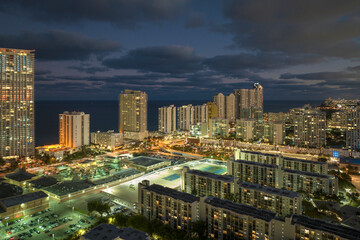 View from above of brightly illuminated high skyscraper buildings in downtown district of Sunny Isles Beach city in Florida, USA. American tourist urban district at night