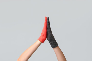 Hands in warm gloves giving high five to each other on grey background