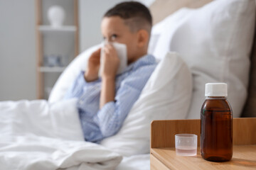 Cough syrup on table of ill little boy in bedroom, closeup