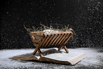 Bible and wooden manger with dummy of baby on black background. Concept of Christmas story