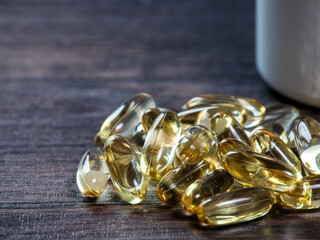 Vitamin D yellow pills on wooden background with soft sun light. Medicine gel pills of vitamin d on table. Yellow Omega 3 oil capsule keeps healthy - medicine concept