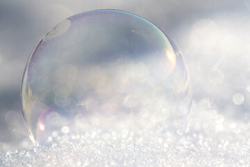 A shimmering soap bubble lies on light-coloured snow. The light shines on the bubble in winter