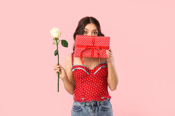 Young shocked Asian woman with beautiful white rose and gift box on pink background