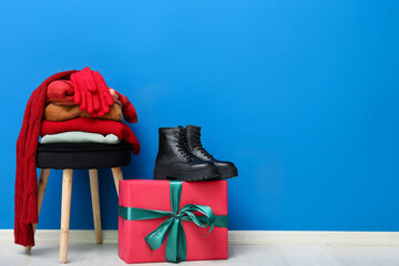Stacked clothes on chair with gift box and boots near blue wall
