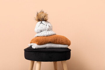 Stack of folded sweaters with hat on chair against beige background