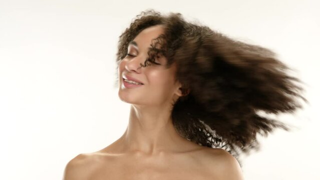 Close up of young pretty woman seductively posing, smiling, shaking fluffy curls, twisting curls on finger, enjoying hairdo. Natural beautiful tanned skin. High quality 4k footage