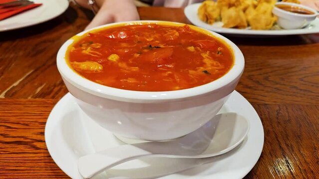 erves red chili soup in a white plate and moves it around the table