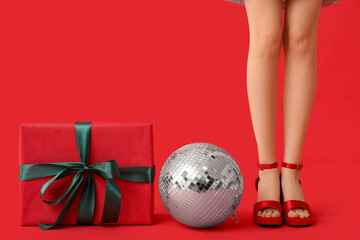 Female legs in trendy high heels with disco ball and gift box on red background